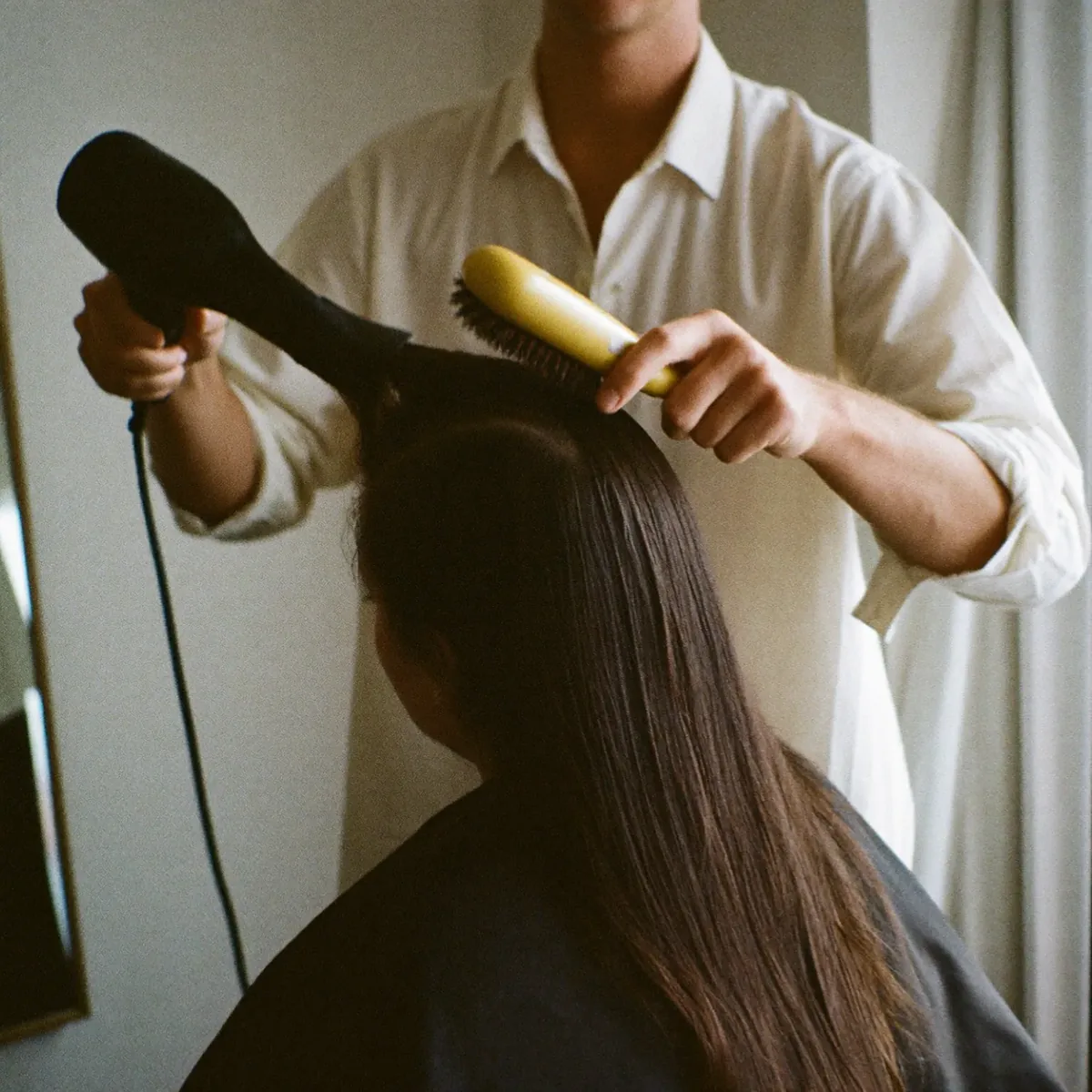 A stylist blow-drying a client's long dark hair in the salon